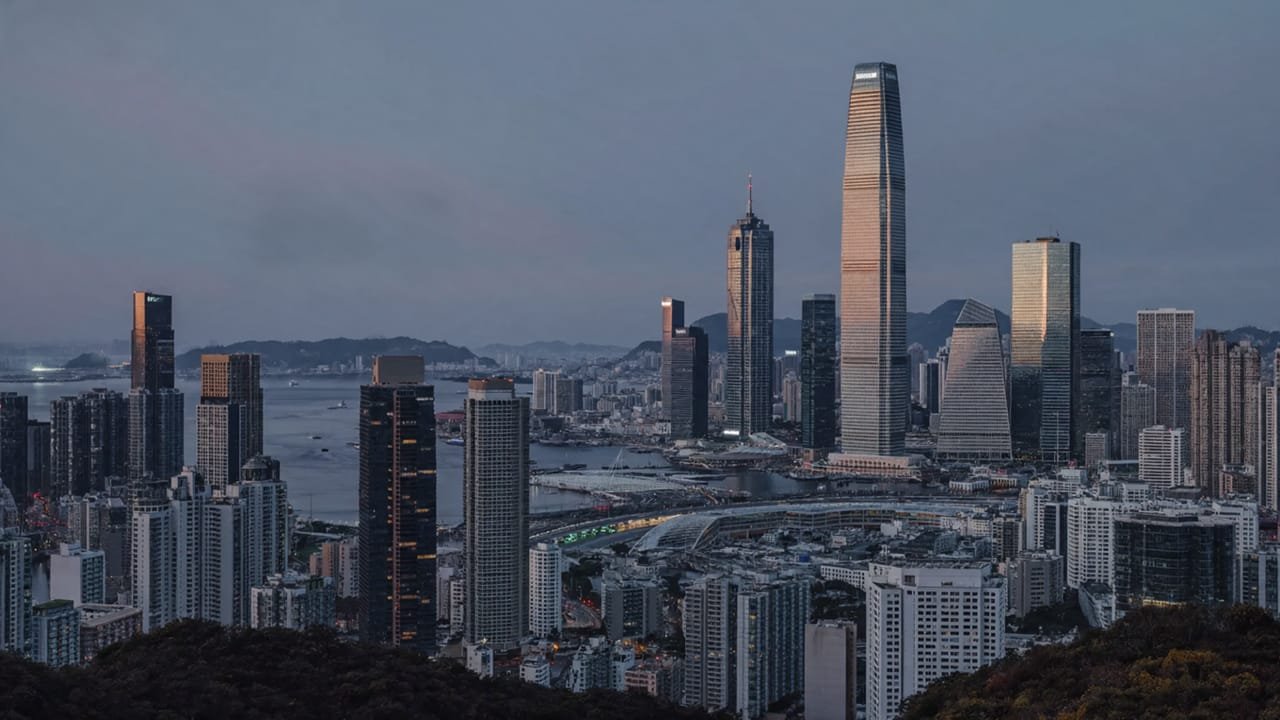 A harbour city skyline at dusk, with high-rise towers along the waterfront and hills beyond.